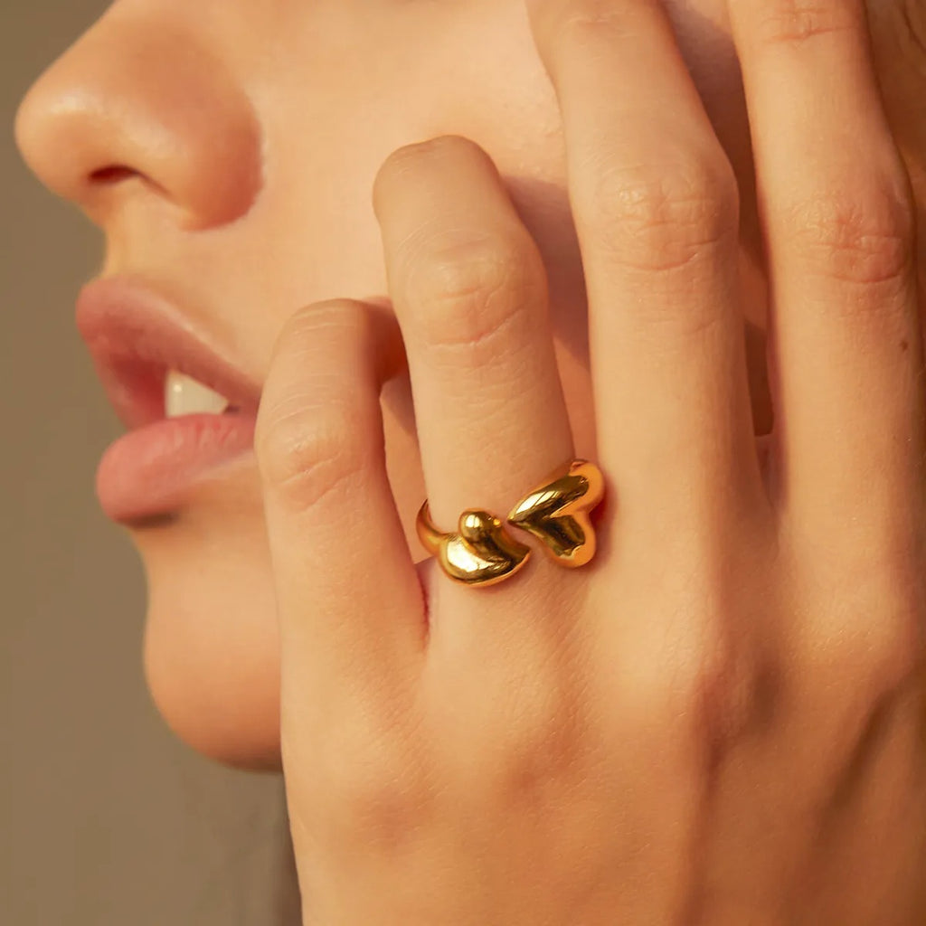 Close-up of a hand wearing a gold ring with heart designs on a neutral background