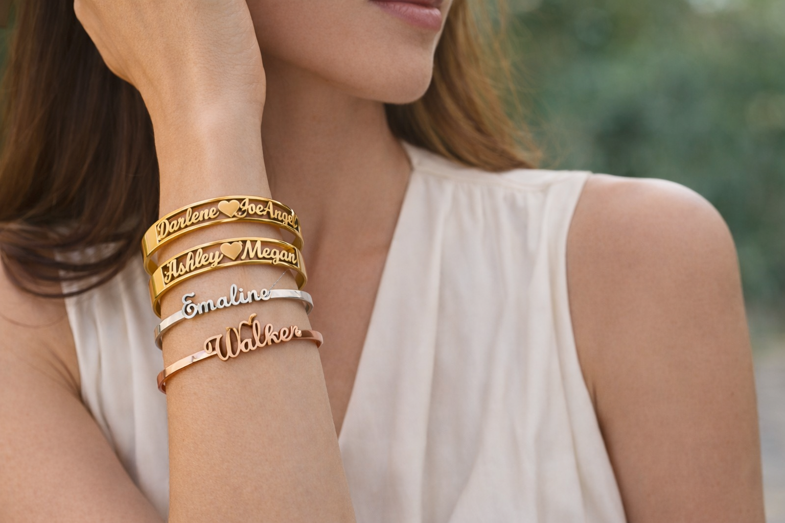 Woman wearing multiple gold name bracelets on a blurred natural background